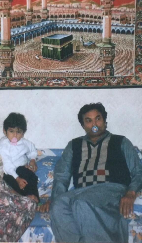 Mukhtar Ahmed on a sofa with a dummy in his mouth, beside his baby who also has a dummy