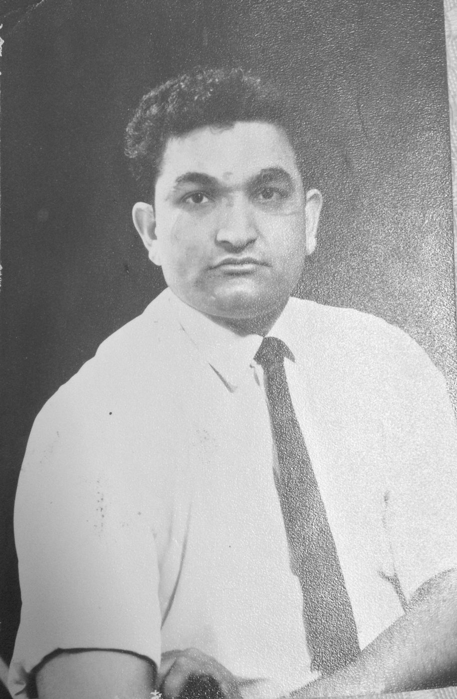 Black and white portrait of a young Mukhtar Ahmed in a white shirt and dark tie